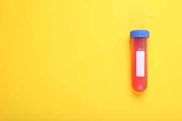 Test tube with liquid on yellow background, top view and space for text. Kids chemical experiment toy