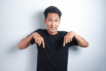 Shocked Asian man wearing black t-shirt pointing at the copy space down below him, isolated by...