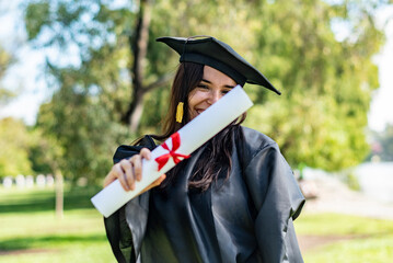 Happy caucasian graduated girl with long brown hair showing her diploma. She is wearing a bachelor...