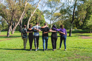 Rear view of a group of friends hugging while walking. Friendship and support concept.