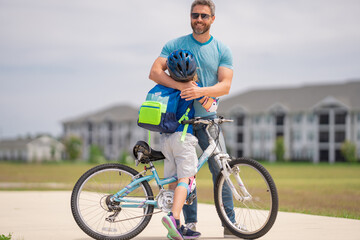 Fototapeta premium Little kid learning to ride bicycle with father in park. Father teaching son cycling. Father and son learning to ride a bicycle at Fathers day. Father support and helping son. Child care.