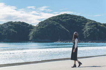 朝日に輝く海の砂浜を歩く女性（静岡県 伊豆 弓ヶ浜）
