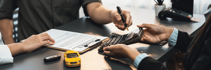 Car dealer calculate interest rate and costs of car loan with calculator, explaining details to customer on term and agreement in dealership office, offering financial and insurance service. Prodigy - obrazy, fototapety, plakaty
