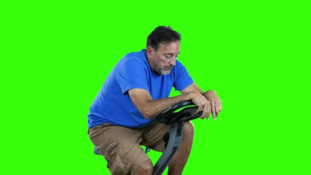 A profile view of an out of shape man pedaling on a stationary exercise bike. Green screen.
