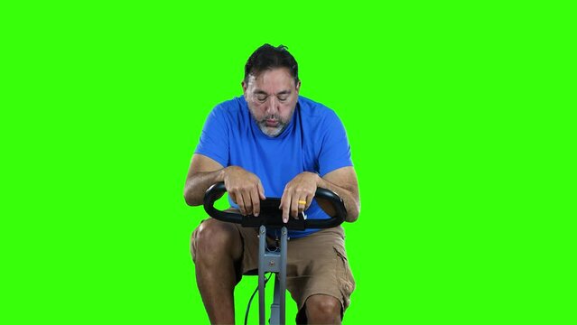 A straight on forward view of a tired man pedaling on a stationary exercise bike. Green screen.
