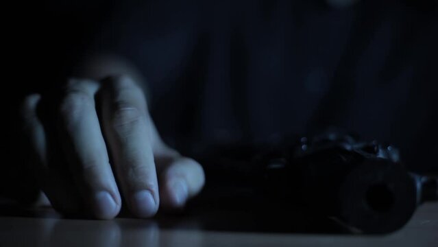 Close-up shot of a man picking up a gun from a table, creative light cinematic shot HD footage.
