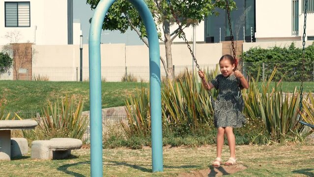 Ni&ntilde;a feliz alegre contenta sonriente disfrutando y jugando en los columpios de un parque infantil al aire libre en un hermoso d&iacute;a soleado al aire libre viviendo su ni&ntilde;ez y su infancia