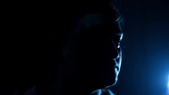 Cinematic shot of a female sitting on a chair with a light on half of his face, dramatic light. HD footage.