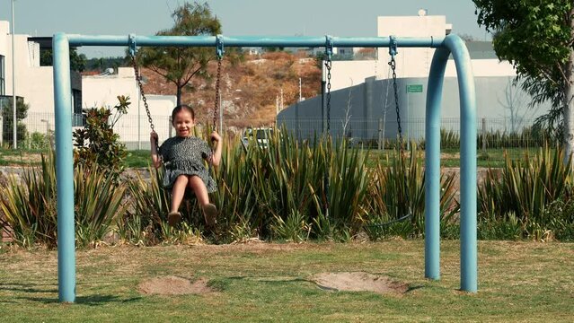Niña feliz alegre contenta sonriente disfrutando y jugando en los columpios de un parque infantil al aire libre en un hermoso día soleado al aire libre viviendo su niñez y su infancia