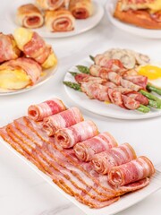 Bacon in a plate, bacon pork rolls in various recipes, on a white kitchen tabletop, indoor scene