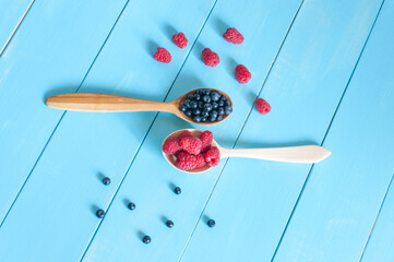 Fresh blueberries and raspberries in wooden spoon. Light blue wood background.