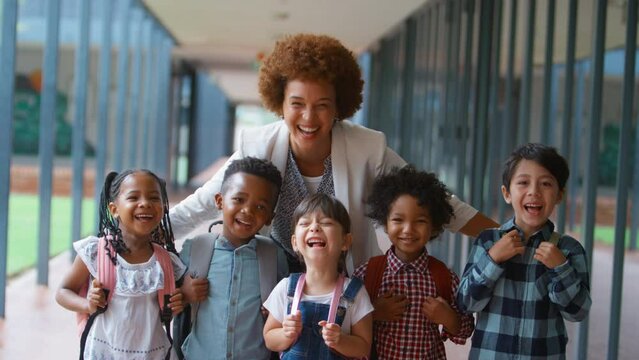 Portrait of class of multi-cultural elementary school students with female teacher standing on outside walkway by school building - shot in slow motion