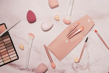 A nude eyeshadow palette and makeup artist's tools on a marble vanity. Brushes for powder, blush, eyebrows, shadows and sponges for concealer and foundation.
