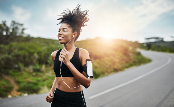 Fitness, sports and happy woman running in a road with music for health, workout or cardio routine. Smile, exercise and African female runner in nature with podcast for training, motivation or energy