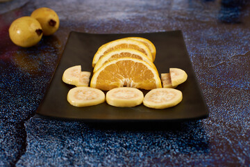 Plate of orange cut into segments, with guavas around it black Plate,