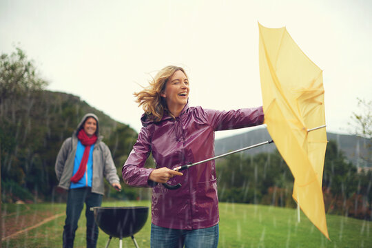 Man, woman and bbq in rain with umbrella, laugh or surprise weather with climate change in garden. Couple, outdoor and funny fail in storm, backyard or cooking in winter with run, wind or hurricane