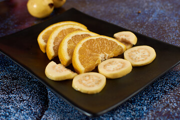 Plate of orange cut into segments, with guavas around it black Plate,