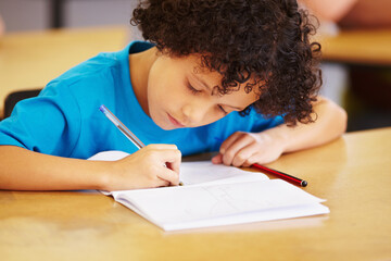 Boy, writing and book in school classroom for learning, focus or development for future. Male...