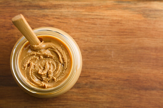 Creamy Smooth Peanut Butter In Jar With Wooden Spoon, Photographed Overhead On Wood With Copy Space On The Side (Selective Focus, Focus On The Peanut Butter)