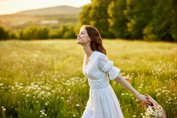 Fototapeta na wymiar happy woman in a light dress and a wicker basket full of daisies enjoys nature walking in the field