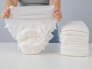 A woman chooses an adult diaper from a pile. Urinary incontinence problem.