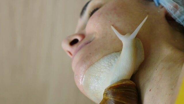 Snails crawling on female face. Vertical footage. Skin care at beauty salon. Anti-aging solutions. Snail with mucin muscus for skin rejuvenation. Beauty, wellness and skin care. korean medicine. 4 k