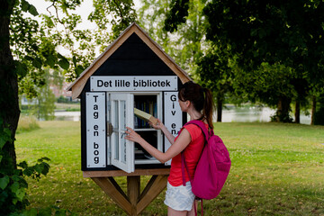 COPENHAGEN. DENMARK – August 14, 2022. A woman borrows a book from a free street library.