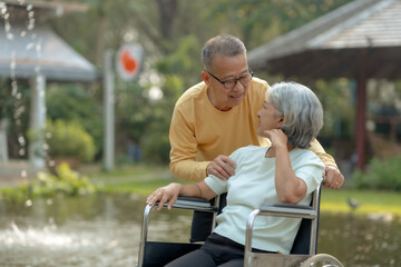 Naklejka premium Asian old man caring for his wife in a wheelchair. Elderly couple. Asian couple giving love to each other smiling happily. Happy Asian senior couple in the park