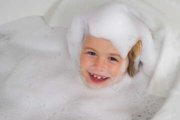 Kid in a bath tub. Washing in bath with soap suds on hair. Child taking bath. Closeup portrait of...
