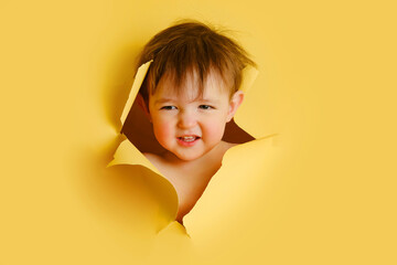 Happy baby in a hole on a paper yellow background. Torn child's head studio background, copy space....