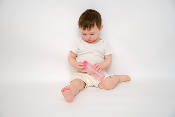 Baby breaks a milk bottle while pressing the nipple, studio white background. Kid about two years...