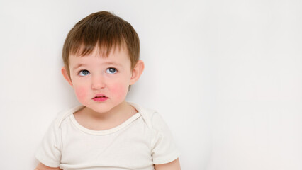 Naklejka premium Thoughtful baby looks up, studio white background. Sad child with the emotion of doubt on his face. Kid about two years old (one year nine months)