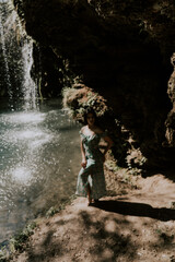 Beautiful model in a turquoise dress posing near a mountain waterfall.Wildlife concept