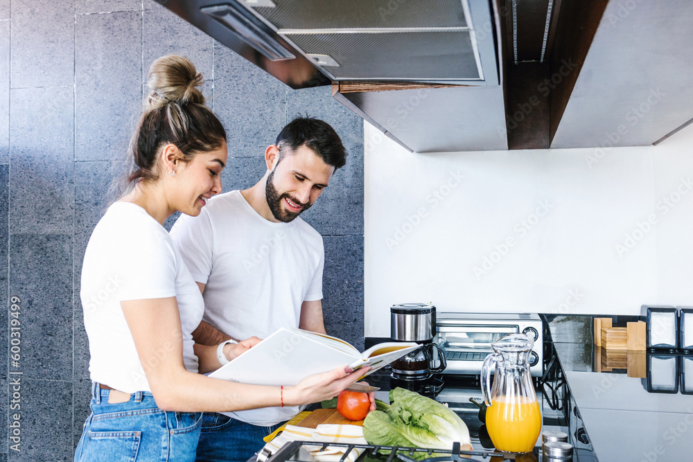 Wall mural young latin couple cooking together in the kitchen healthy food at home in Mexico, Hispanic people	 - Wall murals