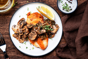 Fried chicken breast with mushrooms and onion sauce with white wine and thyme on plate, old wooden table background, top view