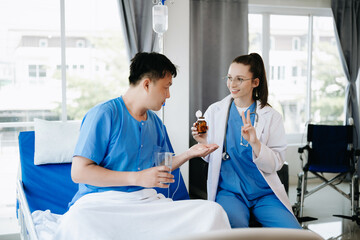 Doctor in white suit take notes while discussing and Asian elderly, man patient who lying on bed with receiving saline solution in hospital or clinic.