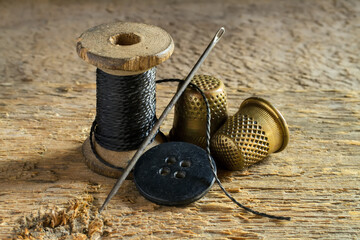 Old sewing utensils on the background of wood. A spool of thread, a button, a needle, thimbles.