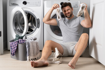 Man with clothes near washing machine. Laundry cleaning. Housework, homework, male housekeeper. Husband man doing laundry at home. Washer and dryer at home.