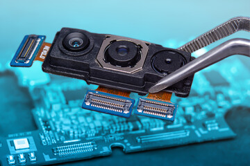 Close-up of a smartphone's triple camera held with tweezers