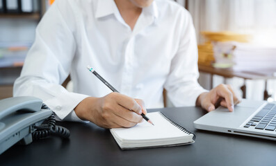 Businessmen talk mobile phones and take notes on their notebooks while working on laptop computers, online business, work from home, teleworking concept.