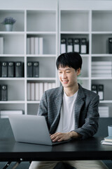 Young Asian businessman working at office with laptop and documents on table.