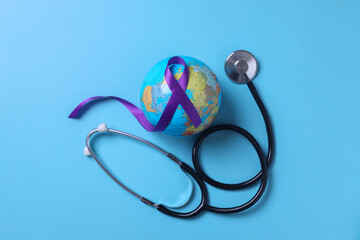 Stethoscope wrapped around globe with purple ribbon cancer awareness on pastel blue background. World cancer day and world epilepsy day