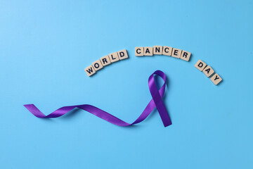 Purple ribbon cancer awareness with world cancer day lettering on alphabetic cube over blue...