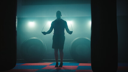 Fototapeta premium Fighter does some jump rope exercises in dark room under light