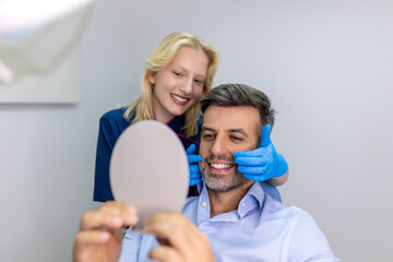 Fototapeta premium Handsome man smiling while looking at mirror in dental clinic. Shot of a Male patient checking her results in the dentists office