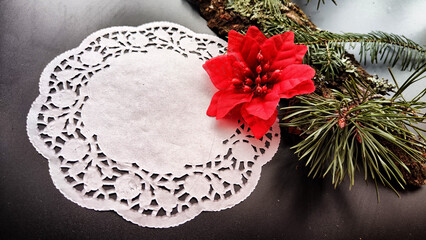 Black frame, white round napkin, green pine branch, red flower on background with reflections and sparkle of light. Abstract location for photo shoot. Cchristmas table decor. Concept of winter holiday