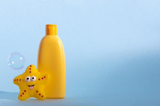 Yellow plastic bottle with baby cosmetic and funny bath toy. Soap bubbles on a background. The concept of children's bath time.