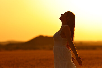 Woman silhouette breathing fresh air in a wheat field at sunset