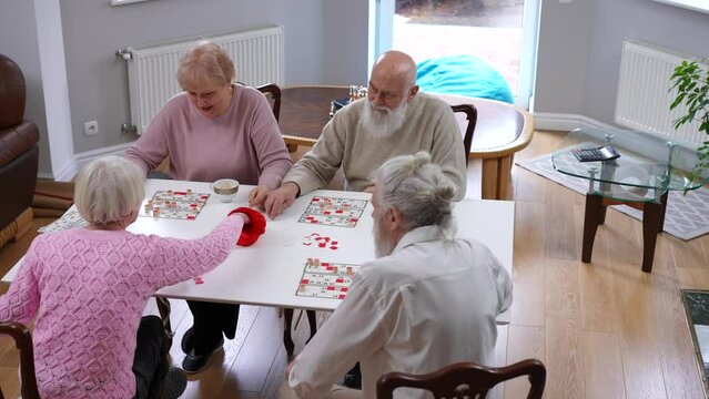 High angle view group of curious old men and women playing table lotto indoors. Wide shot positive active Caucasian elderly friends enjoying leisure having fun in living room