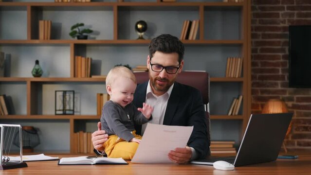 Businessman in formal clothes is working indoors. With toddler on the table.
